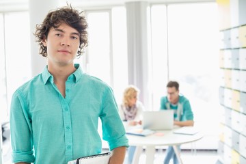 Portrait of confident businessman with colleagues working in background at creative office