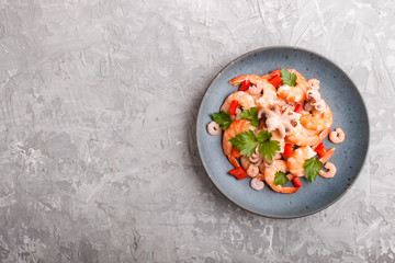 Boiled shrimps or prawns and small octopuses with herbs on a blue ceramic plate on a gray concrete background. Top view.