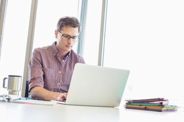 Mid-adult businessman working laptop at desk in creative office