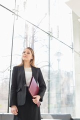 Confident businesswoman looking away while holding folder at office lobby