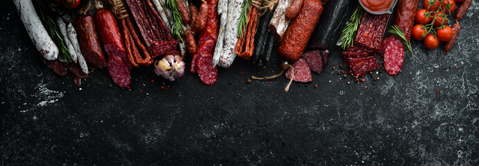 Background of salami, sausages and meat products, on black stone background. Top view. Free space...