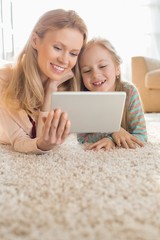 Happy mother and daughter using digital tablet on floor at home