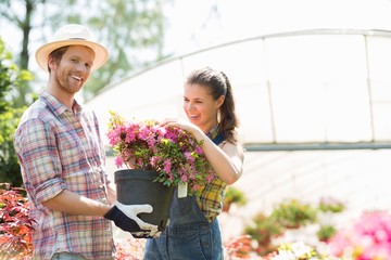 Happy gardeners holding flower pot outside greenhouse