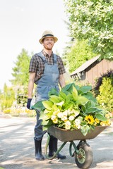 Full-length of gardener pushing wheelbarrow with plants at garden