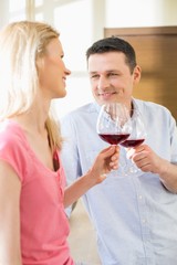 Happy couple toasting red wine glasses in kitchen