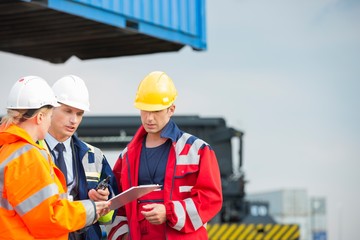 Workers discussing over clipboard in shipping yard