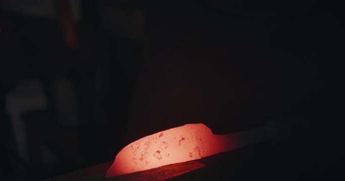 Blacksmith hammering heated iron on anvil making knife dark and eerie