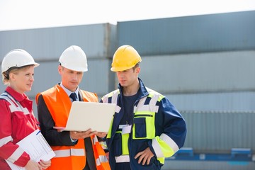 Fototapeta premium Workers discussing over laptop in shipping yard
