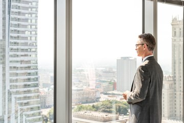 Fototapeta premium Side view of mature businessman looking through office window