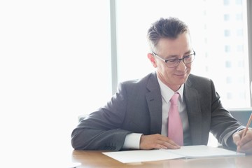 Mature businessman writing on book at table in office
