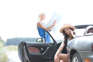 Woman using cell phone in convertible while friend reading map on road