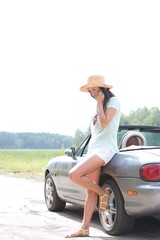 Full-length of woman using cell phone while leaning on convertible at countryside