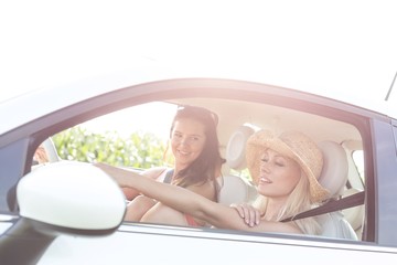 Young female friends in car on sunny day against clear sky
