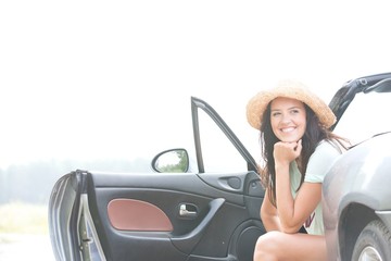 Happy woman sitting in convertible against clear sky