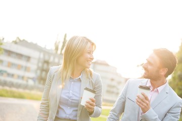 Happy business couple conversing while holding disposable cups in city