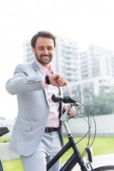 Happy businessman with bicycle checking time outdoors