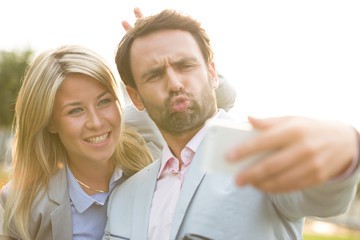 Playful business couple taking selfie outdoors on sunny day