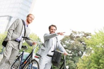 Smiling businessman with bicycle showing something to colleague on street