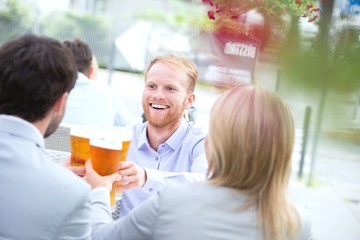 Fototapeta na wymiar Happy businessman toasting beer glass with colleagues at outdoor restaurant