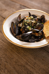 Fototapeta na wymiar Mussels in white wine sauce with herbs in a bowl with golden croutons on a dark, wooden board.