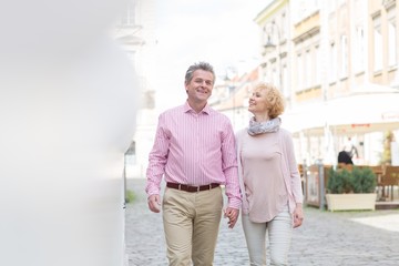 Happy middle-aged couple talking while walking in city
