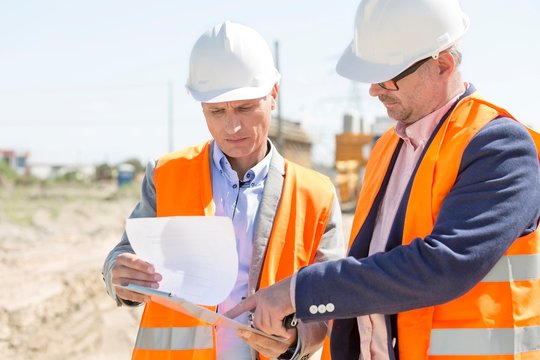 Engineers examining documents on clipboard at construction site against clear sky