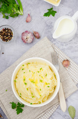 Mashed potatoes with butter, milk, garlic and green onions in a bowl on a gray background. A traditional dish of Ukrainian, Russian cuisine. Top view. Vertical orientation.