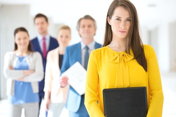 Portrait of confident young businesswoman with team in background at office