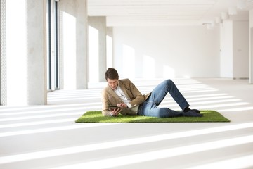 Full length of young businessman using digital tablet while reclining on turf in office