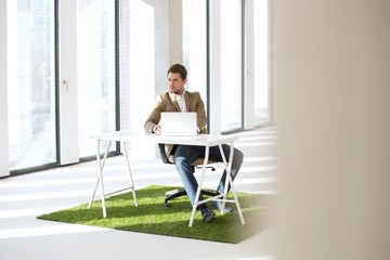 Full length of young businessman with laptop at desk on turf in new office