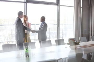 Businessmen shaking hands by female colleague in conference room at office