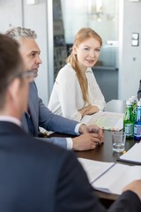 Obraz premium Portrait of young businesswoman sitting with male colleagues in conference room