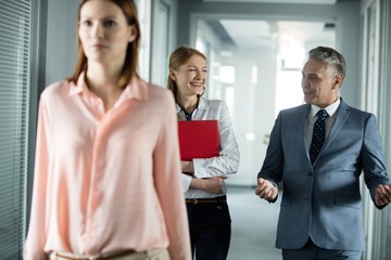 Businessman and businesswoman talking while walking in corridor with female colleague in foreground at office