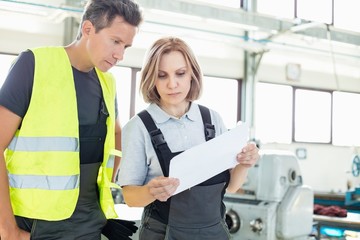 Male and female manual workers examining paper in industry