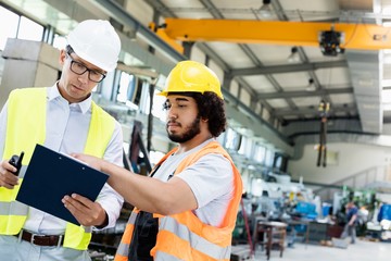 Supervisor with manual worker discussing over clipboard in metal industry