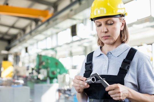 Mature female worker measuring metal with caliper in industry - Powered by Adobe