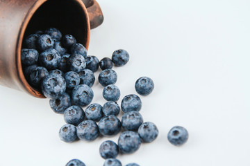  A bunch of ripe blueberries on a white background copy space. Blueberries spilling out of a stein.