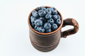  Brown clay mug filled with ripe blueberries on a white background copy space. Harvesting blueberries. Berry breakfast. Folk stein with berry.