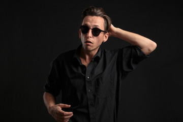 Confident stylish man in black eyeglasses fixing hair isolated over black background.