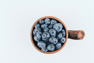  Brown clay mug filled with ripe blueberries on a white background copy space. Harvesting blueberries. Berry breakfast. Folk stein with berry.