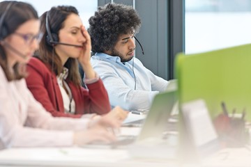 Tired male customer service representative with colleagues working in office