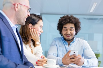 Smiling young businessman using mobile phone with colleagues in office