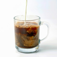 milk poured into a transparent cup of black coffee