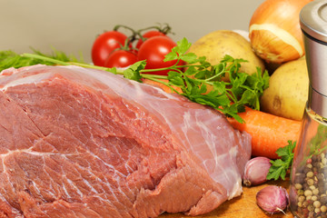 A large piece of raw pork is surrounded by several vegetables