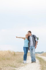 Young woman showing something to man while standing on trail at field