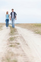 Full length of young hiking couple walking on trail at field