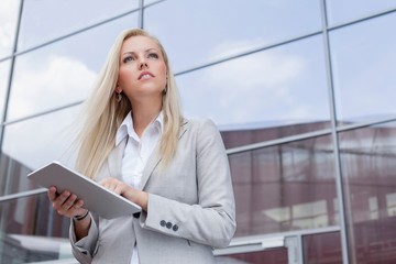 Low angle view of businesswoman holding digital tablet while looking away against office building