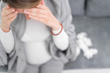 Pregnant woman catching cold, flu, virus, sitting at home on a couch, blowing nose and being sick.