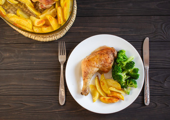 Roasted chicken legs served with potatoes and broccoli pictured from above. Top view.