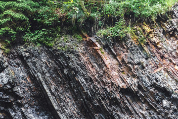 Multilayered dark rocky geological layers on the bank of a mountain river. Rock with visible...